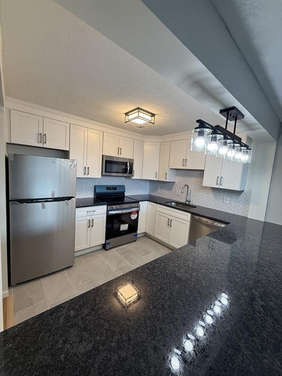 kitchen with appliances with stainless steel finishes, dark stone counters, sink, light tile patterned floors, and white cabinetry