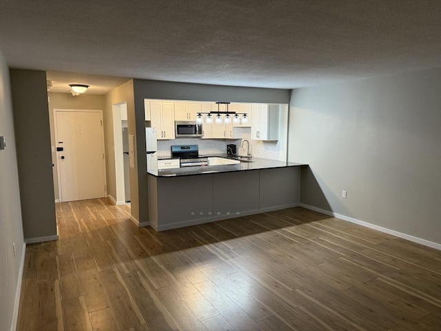 kitchen with kitchen peninsula, white cabinets, wood-type flooring, and appliances with stainless steel finishes