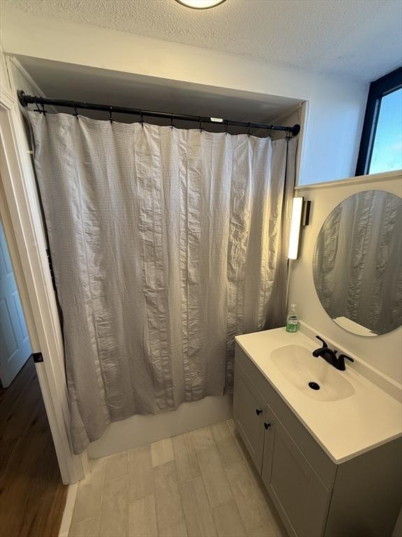 bathroom with hardwood / wood-style floors, shower / bath combination with curtain, a textured ceiling, and vanity