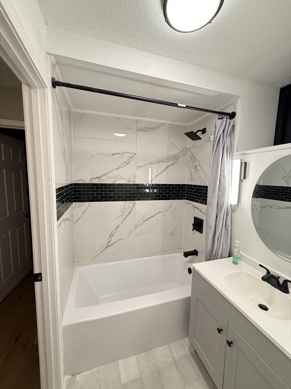 bathroom featuring vanity, shower / bathtub combination with curtain, and a textured ceiling