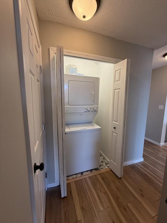 washroom with a textured ceiling, stacked washer / dryer, and dark hardwood / wood-style floors