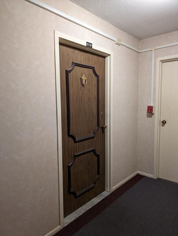 doorway to outside with dark colored carpet and a textured ceiling