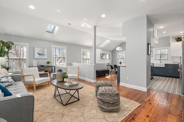 living room with plenty of natural light, sink, vaulted ceiling with skylight, and light hardwood / wood-style flooring