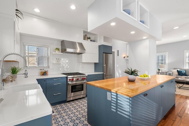 kitchen with a kitchen island, butcher block countertops, premium appliances, blue cabinetry, and wall chimney exhaust hood