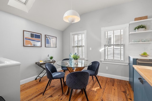 dining room with lofted ceiling with skylight and light hardwood / wood-style floors