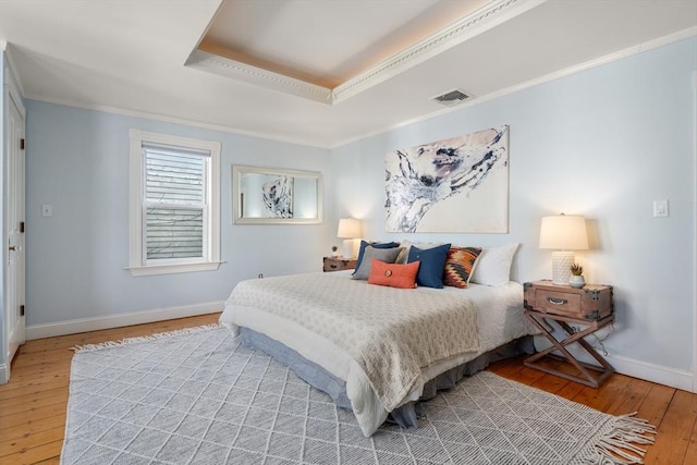 bedroom featuring a raised ceiling, crown molding, and hardwood / wood-style flooring