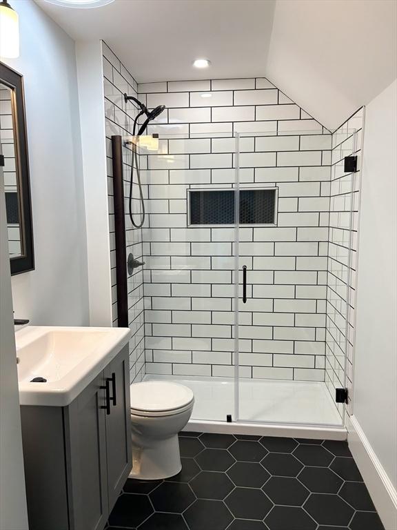 bathroom with vanity, vaulted ceiling, tile patterned flooring, toilet, and walk in shower