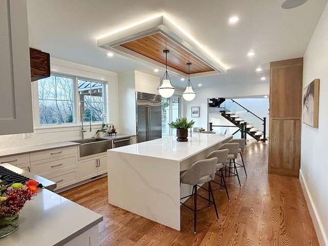 kitchen with a center island, sink, light wood-type flooring, white cabinetry, and stainless steel built in refrigerator