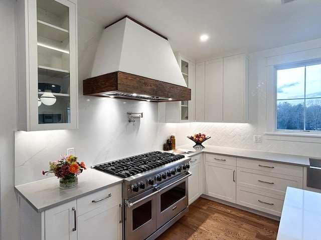 kitchen with white cabinets, range with two ovens, premium range hood, and dark wood-type flooring