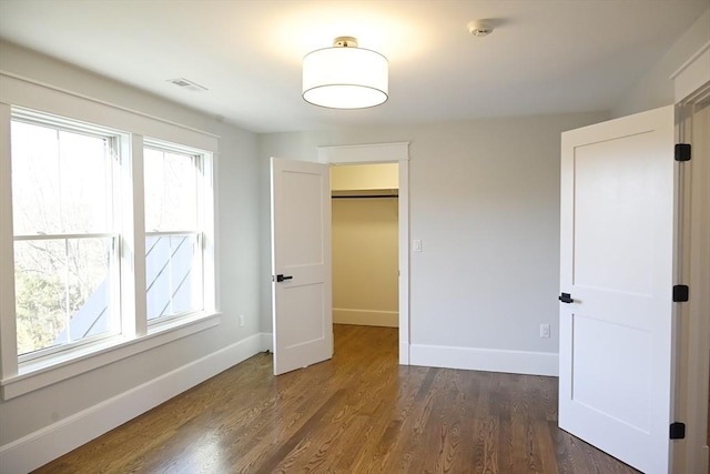 unfurnished bedroom with multiple windows, a closet, dark hardwood / wood-style flooring, and a spacious closet