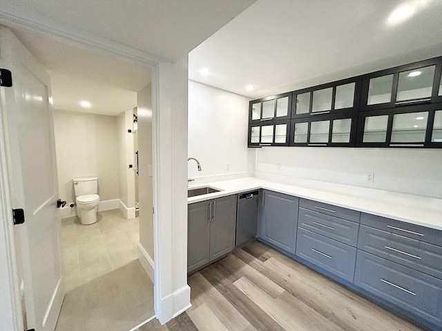 bar with sink, stainless steel dishwasher, and light wood-type flooring