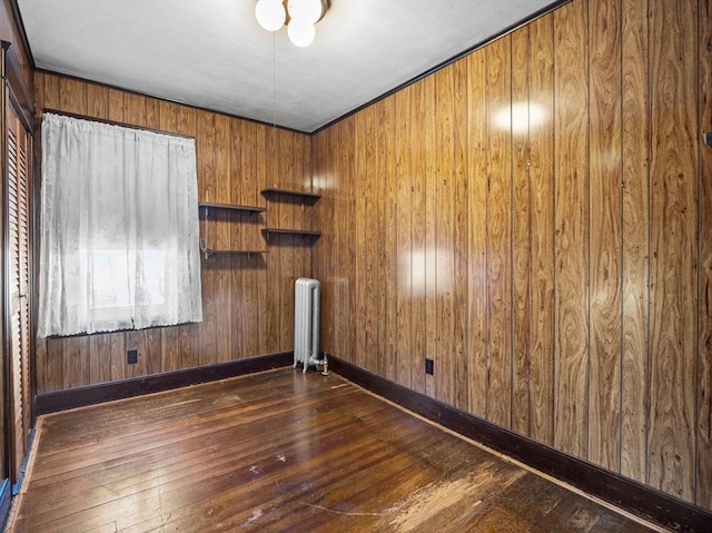 empty room featuring dark hardwood / wood-style floors, radiator heating unit, and wood walls