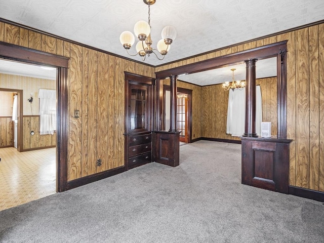 carpeted spare room featuring an inviting chandelier, a wealth of natural light, wooden walls, and ornate columns