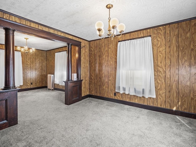 empty room featuring an inviting chandelier, radiator heating unit, decorative columns, and carpet