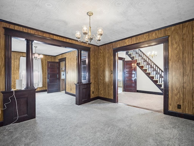 carpeted spare room with an inviting chandelier, ornate columns, and wood walls