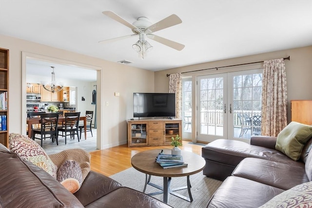 living area featuring visible vents, baseboards, light wood-style flooring, french doors, and ceiling fan with notable chandelier