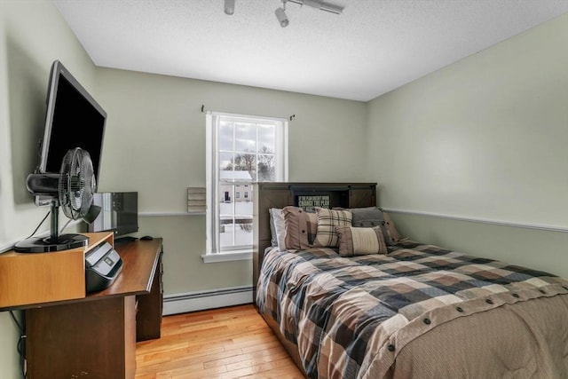 bedroom featuring baseboard heating, light hardwood / wood-style flooring, and a textured ceiling