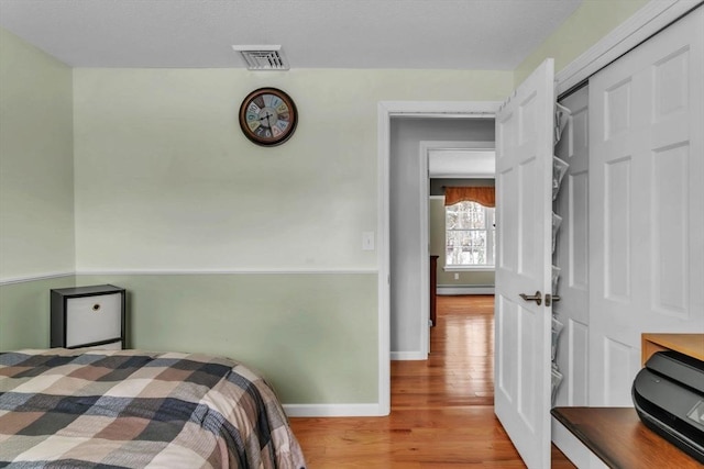 bedroom with a baseboard heating unit, hardwood / wood-style flooring, and a closet