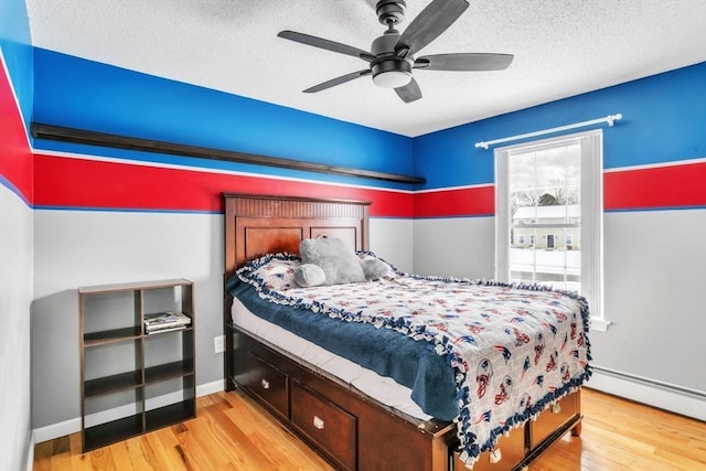 bedroom with ceiling fan, light hardwood / wood-style floors, a textured ceiling, and baseboard heating