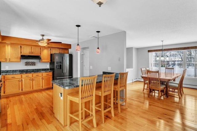 kitchen featuring pendant lighting, a kitchen bar, light wood-type flooring, and black fridge