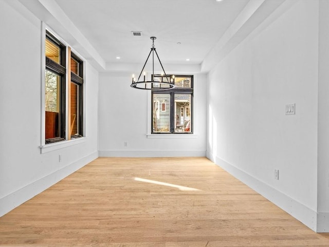 unfurnished dining area featuring an inviting chandelier, a raised ceiling, and light wood-type flooring