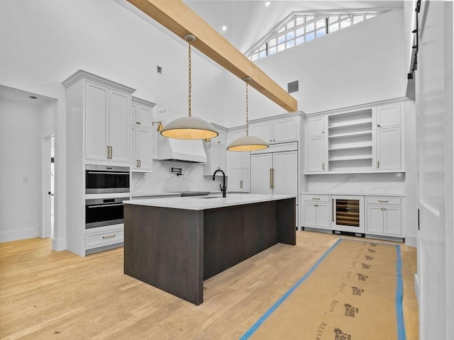 kitchen featuring pendant lighting, stainless steel oven, a kitchen island with sink, and white cabinets