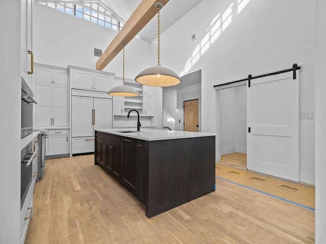 kitchen with sink, paneled built in refrigerator, an island with sink, pendant lighting, and a barn door