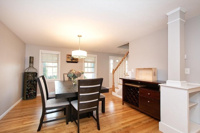 dining room featuring light wood-type flooring, ornate columns, baseboards, and stairway