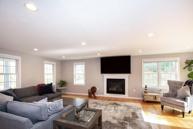 living area with light wood-type flooring, recessed lighting, baseboards, and a glass covered fireplace