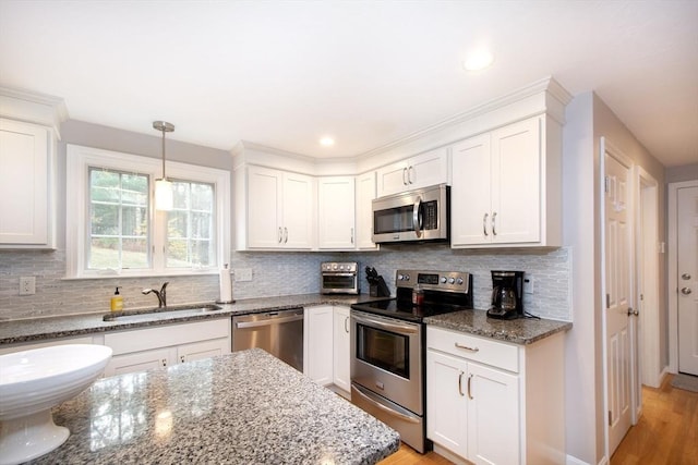 kitchen with tasteful backsplash, appliances with stainless steel finishes, white cabinetry, a sink, and dark stone countertops