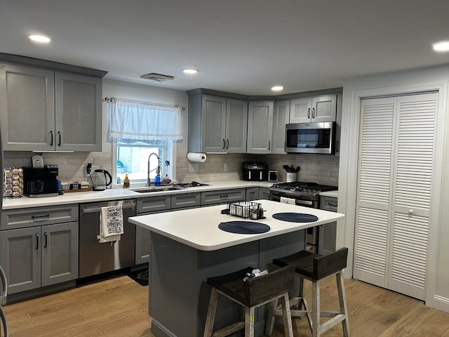 kitchen featuring a sink, appliances with stainless steel finishes, light wood finished floors, and gray cabinets