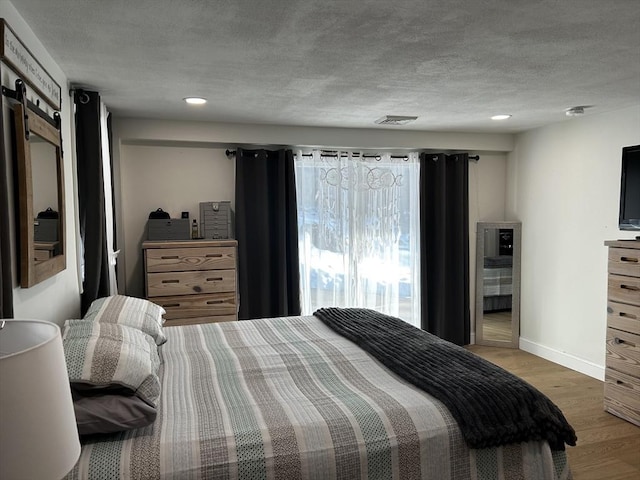 bedroom featuring light wood finished floors, baseboards, visible vents, a textured ceiling, and recessed lighting