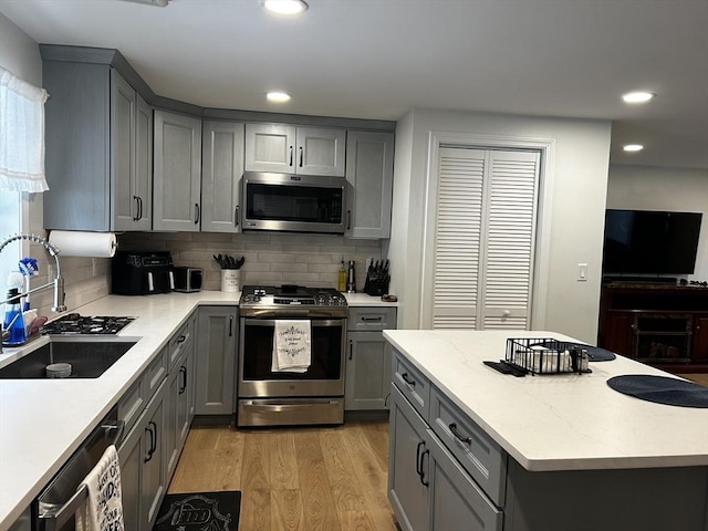 kitchen with appliances with stainless steel finishes, a sink, light wood-style flooring, and gray cabinetry