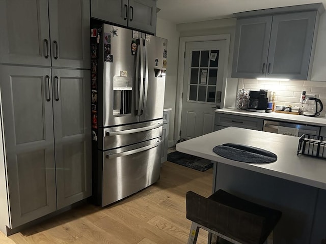 kitchen featuring light countertops, light wood-type flooring, stainless steel fridge, and decorative backsplash