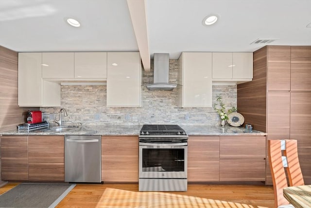 kitchen with decorative backsplash, light wood-type flooring, stainless steel appliances, light stone counters, and wall chimney exhaust hood