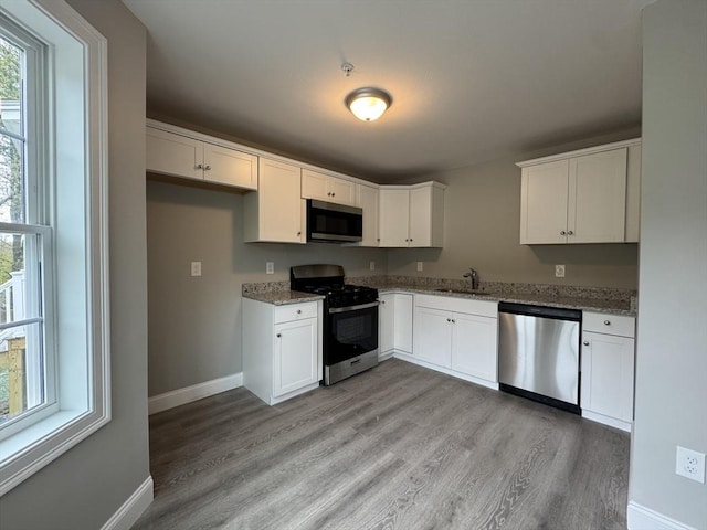 kitchen with light wood-type flooring, white cabinetry, appliances with stainless steel finishes, and light stone counters