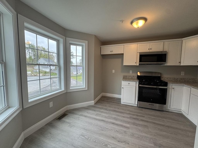 kitchen with light stone counters, white cabinetry, light wood finished floors, and stainless steel appliances