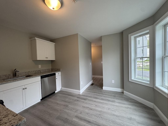 kitchen featuring stainless steel dishwasher, light stone countertops, white cabinets, a sink, and light wood-style flooring