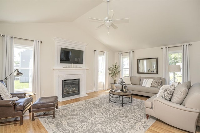 living room featuring ceiling fan, light hardwood / wood-style flooring, a premium fireplace, and vaulted ceiling