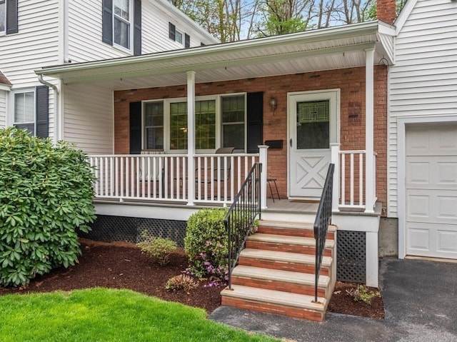 view of exterior entry with a chimney, brick siding, covered porch, and an attached garage