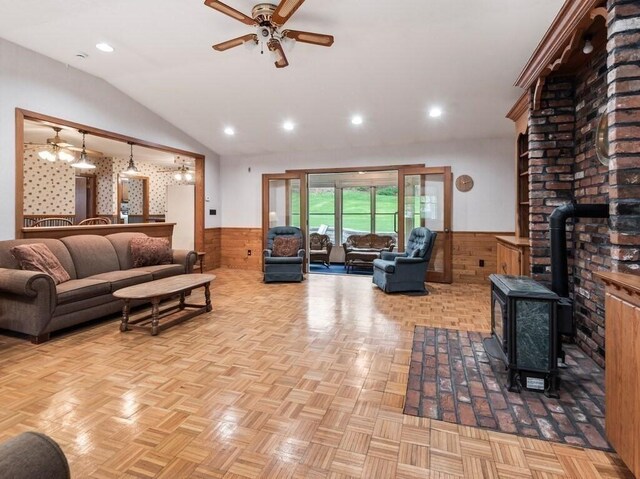 living area featuring a wood stove, lofted ceiling, wainscoting, and ceiling fan