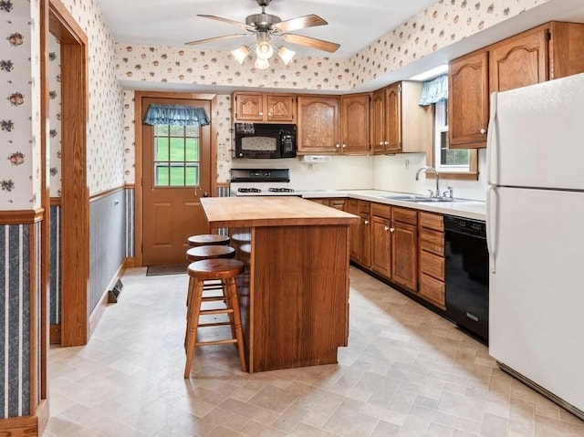 kitchen with a sink, black appliances, a ceiling fan, wooden counters, and wallpapered walls