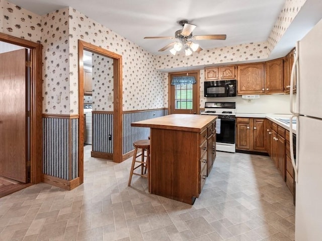 kitchen with wainscoting, black microwave, gas range, and wallpapered walls