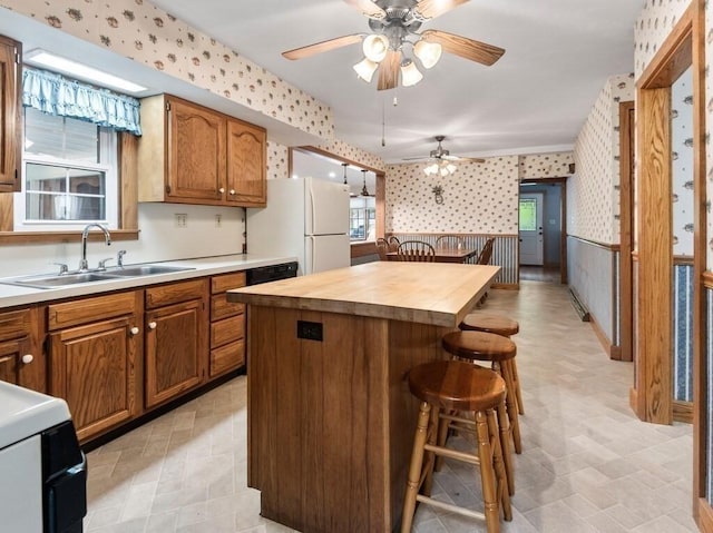 kitchen with a ceiling fan, wallpapered walls, a sink, and a kitchen bar