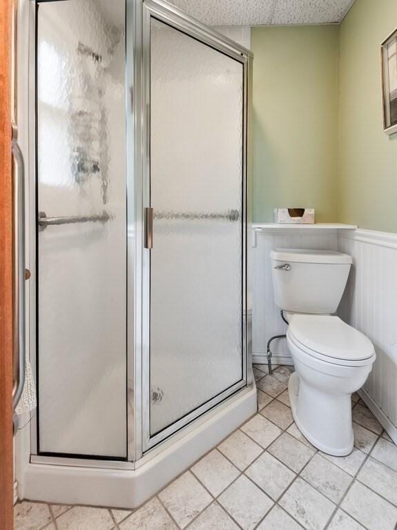 bathroom with a shower stall, tile patterned floors, toilet, and a wainscoted wall
