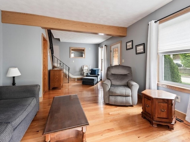 living area with beam ceiling, stairway, light wood-style flooring, and baseboards