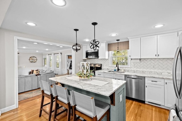 kitchen with tasteful backsplash, a sink, open floor plan, stainless steel appliances, and white cabinetry