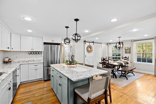kitchen with decorative backsplash, a barn door, white cabinetry, stainless steel appliances, and light wood-style flooring