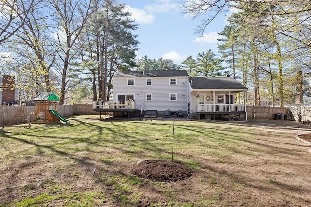 back of property featuring a lawn, a wooden deck, a fenced backyard, and a playground