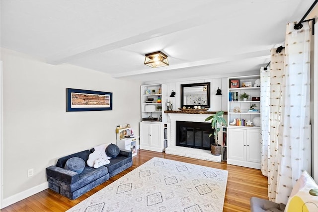 living room featuring baseboards, beam ceiling, a brick fireplace, and wood finished floors